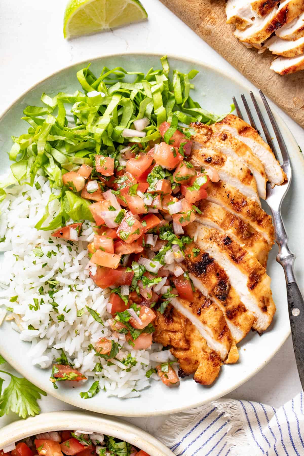 Grilled chicken on a white plate with rice, pico de gallo, and shredded lettuce. 