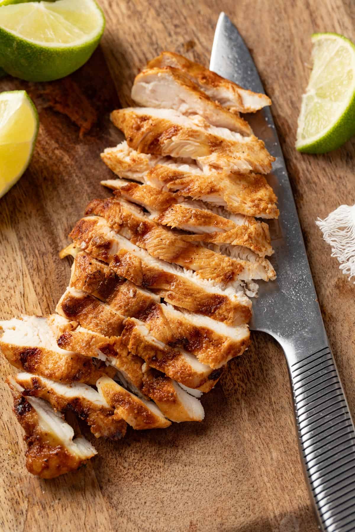 A cutting board with sliced chicken on top next to a knife. 