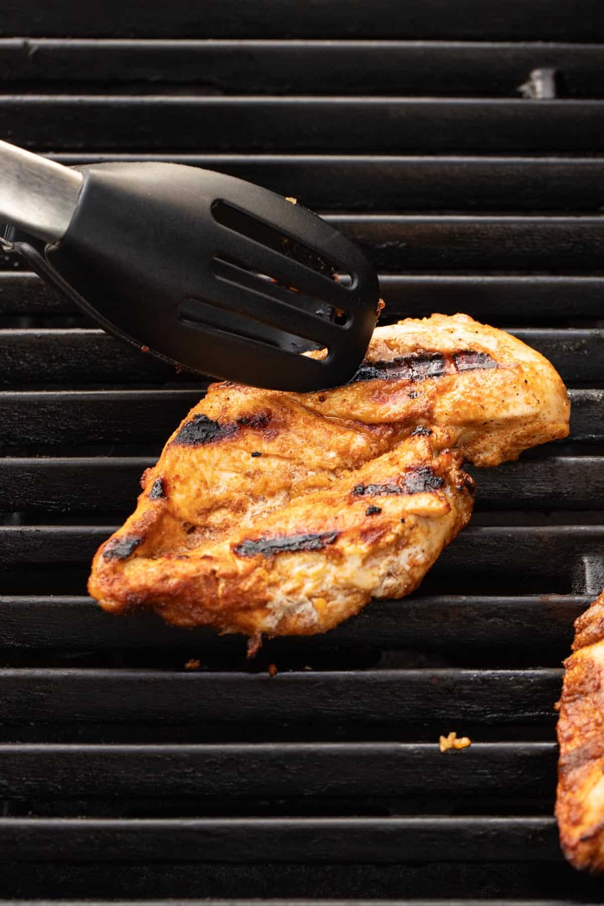 A marinated chicken breast being grilled with tongs flipping it over. 