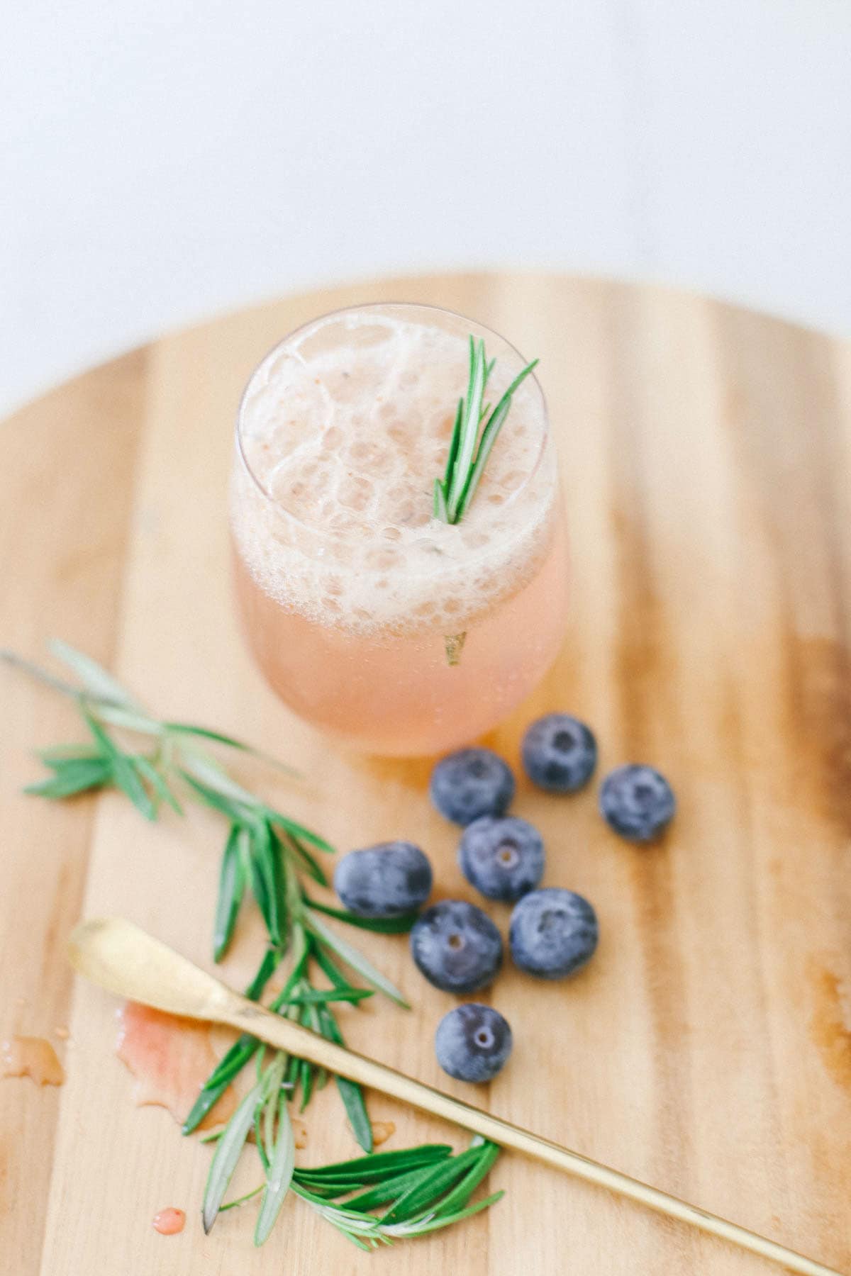 Blueberries next to a drink with a gold cocktail stirrer.