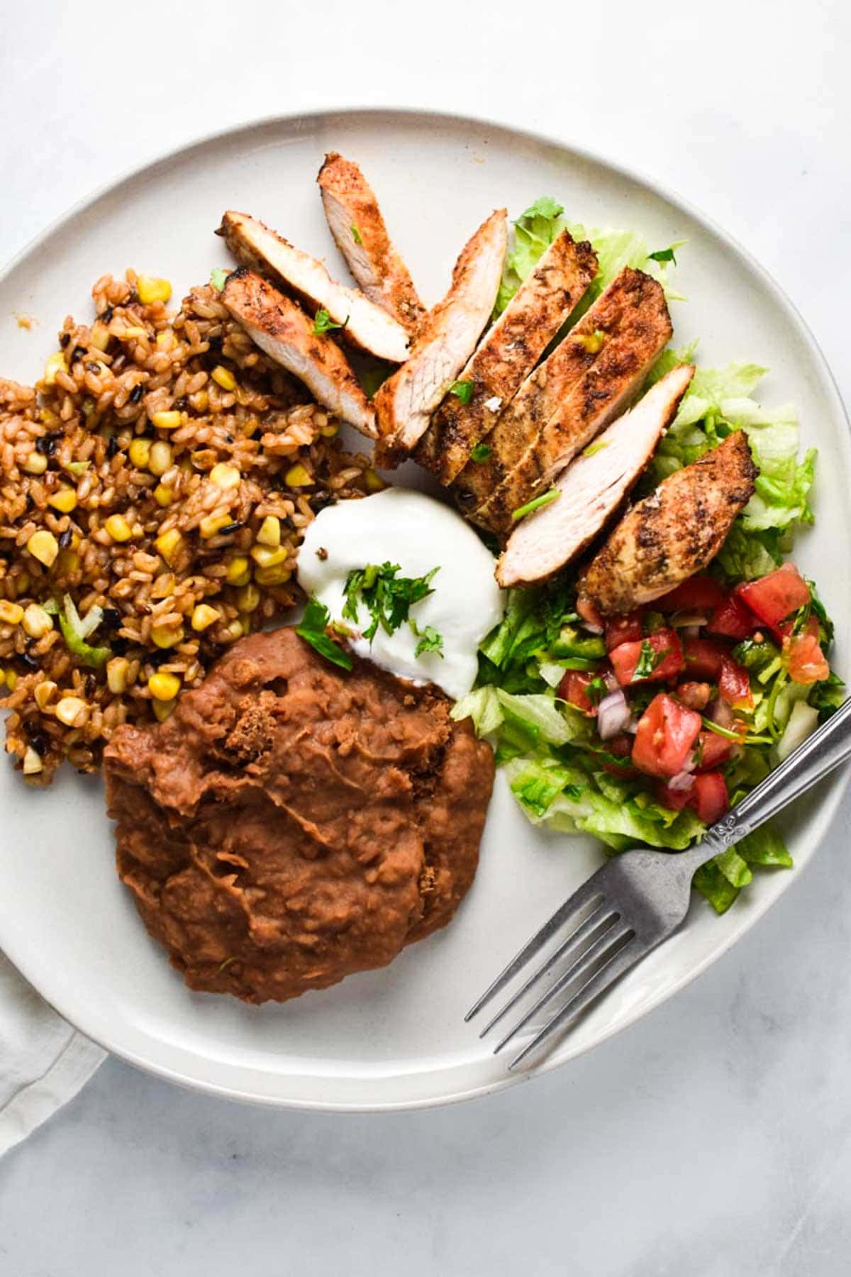 A plate of grilled chicken on top of lettuce and tomatoes.