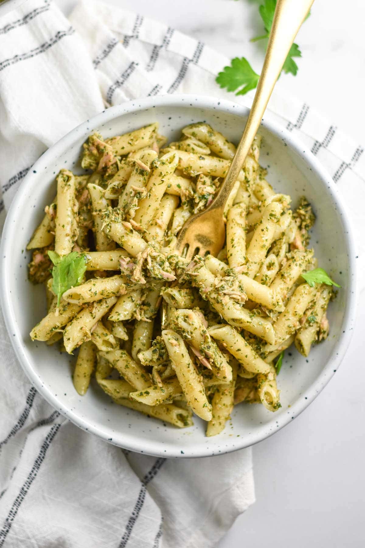 A large bowl of pasta with pesto and parsley on a striped towel.