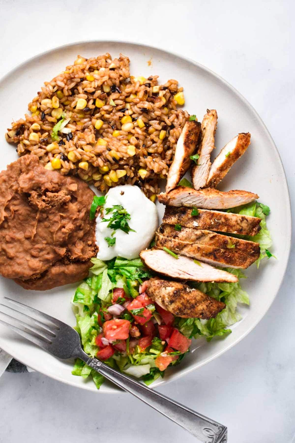 Sliced grilled chicken next to refried beans and Mexican rice.