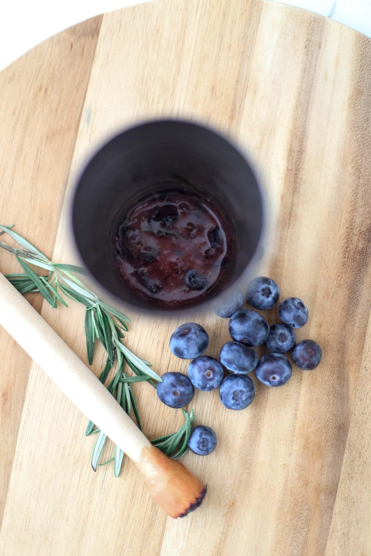 Muddling blueberries and herbs in a cocktail shaker.