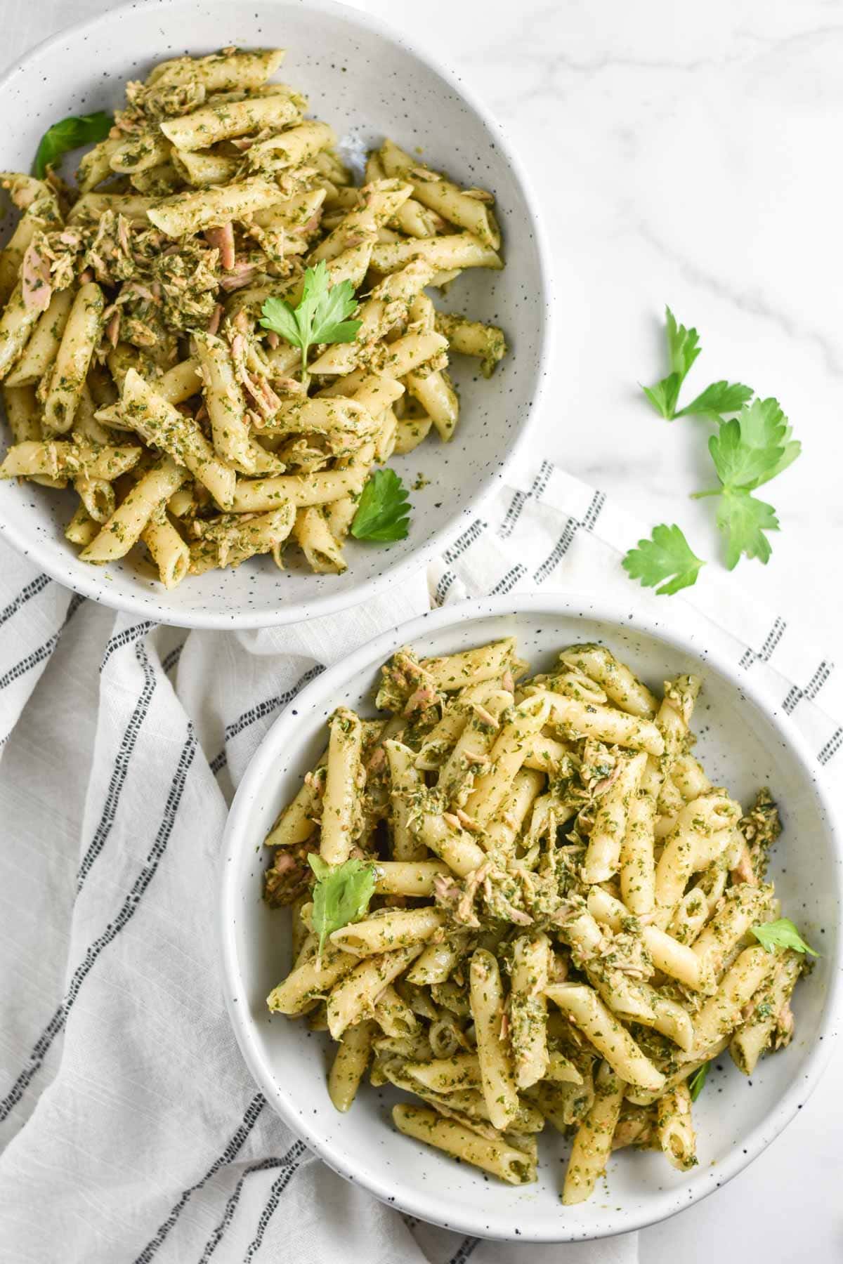 Two white bowls filled with tuna pasta and parsley.