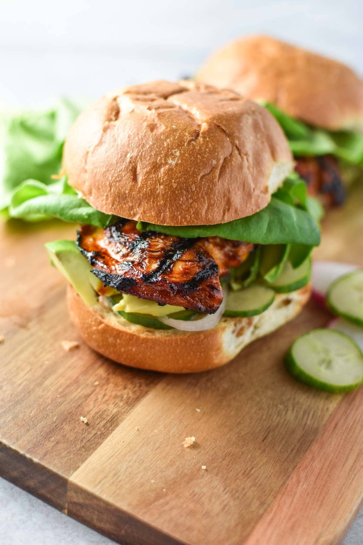 A grilled chicken sandwich on a wood serving platter.