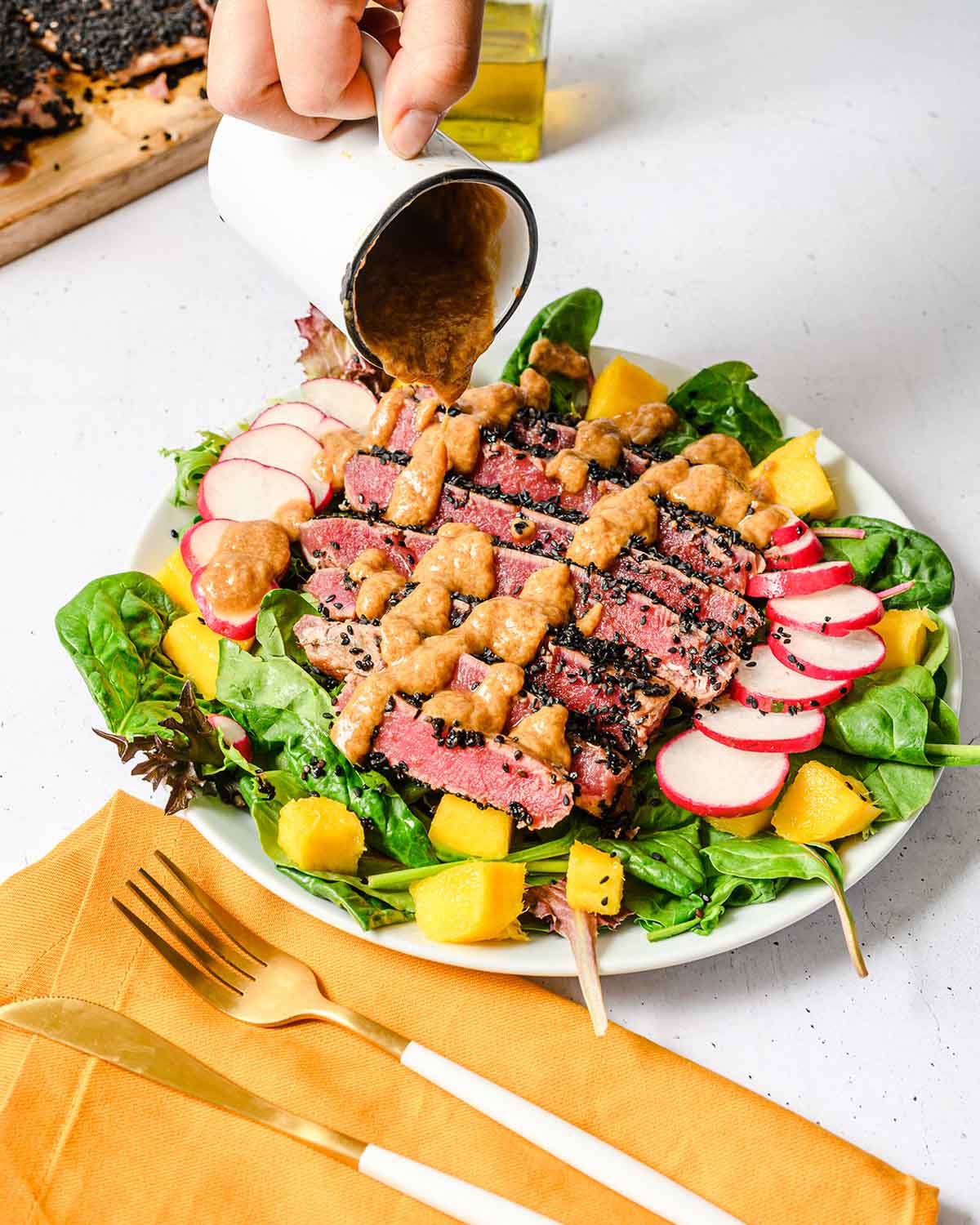 Sesame dressing being pouring on top of a salad with ahi tuna.