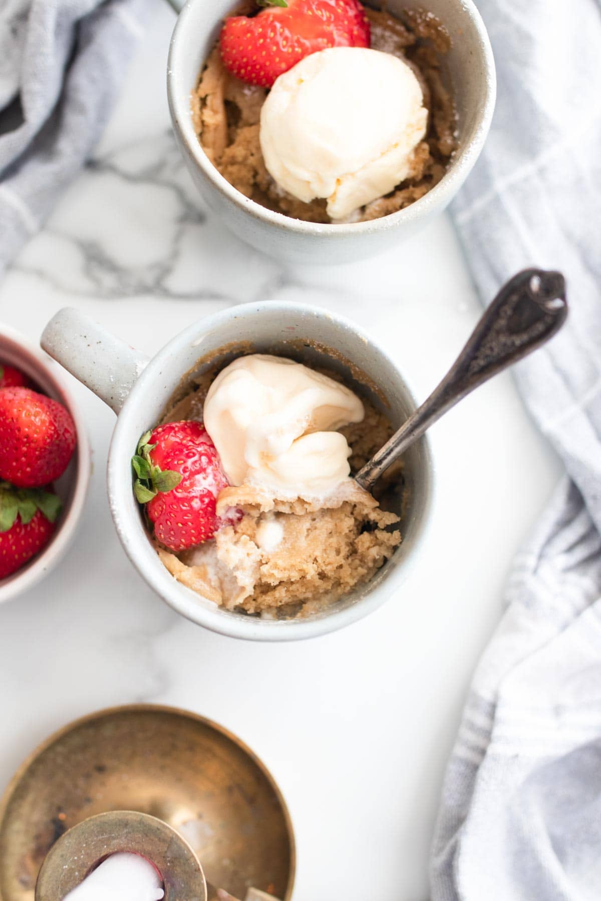 Melted vanilla ice cream on top of two mug cakes with strawberries.