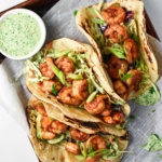 Healthy shrimp tacos next to a bowl of creamy cilantro sauce.