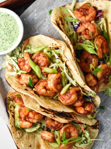 Healthy shrimp tacos next to a bowl of creamy cilantro sauce.