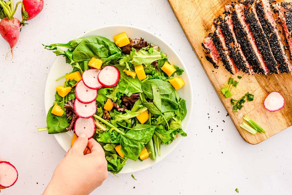 Placing radish and mango on top of a bowl of greens. 