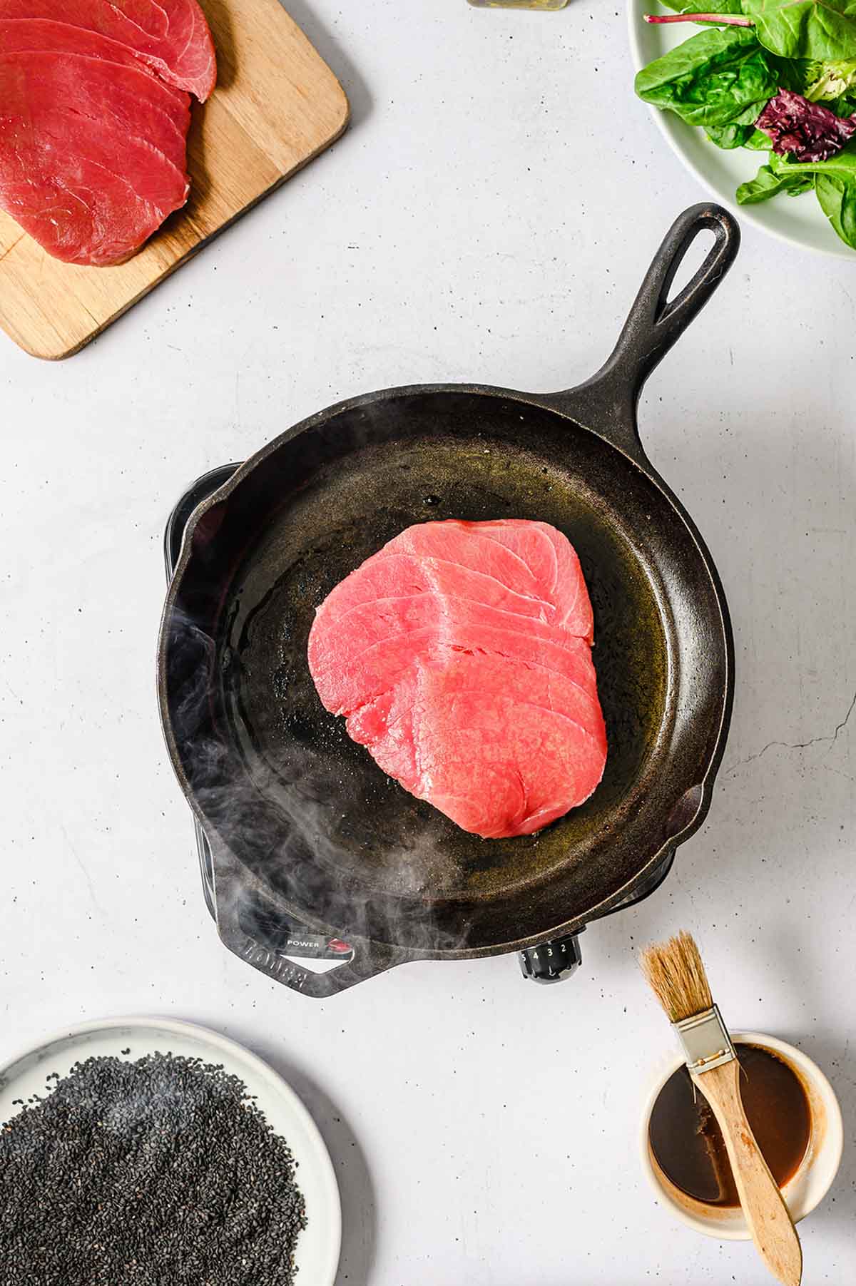 Raw ahi tuna in a cast iron pan next to sauce.