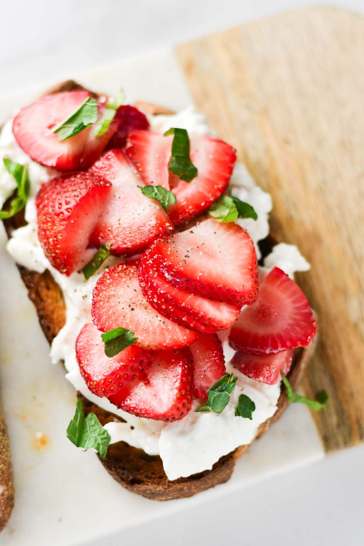 A toast topped with strawberries, burrata, and mint.