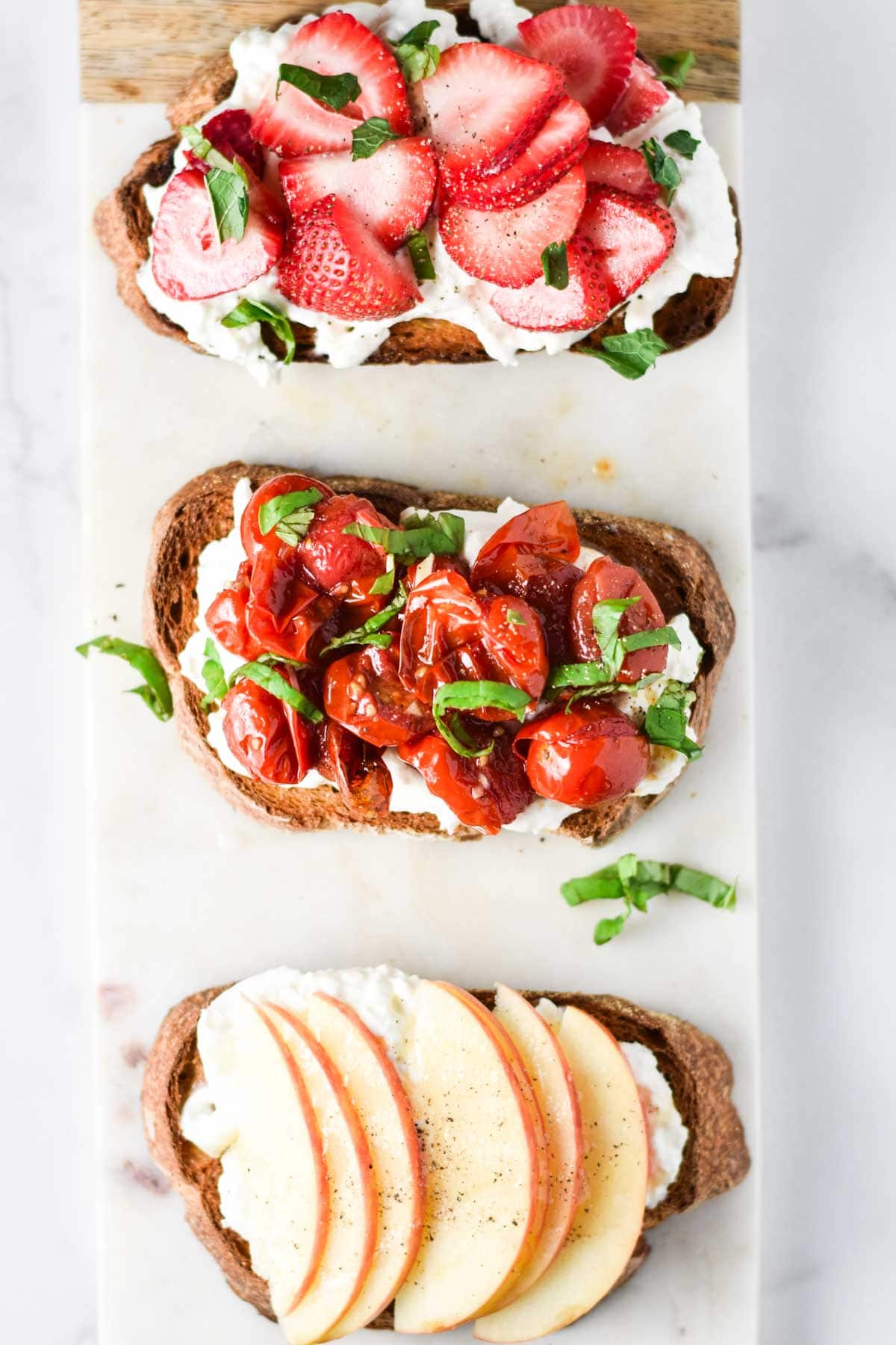Three burrata toasts topped with fruits and herbs.