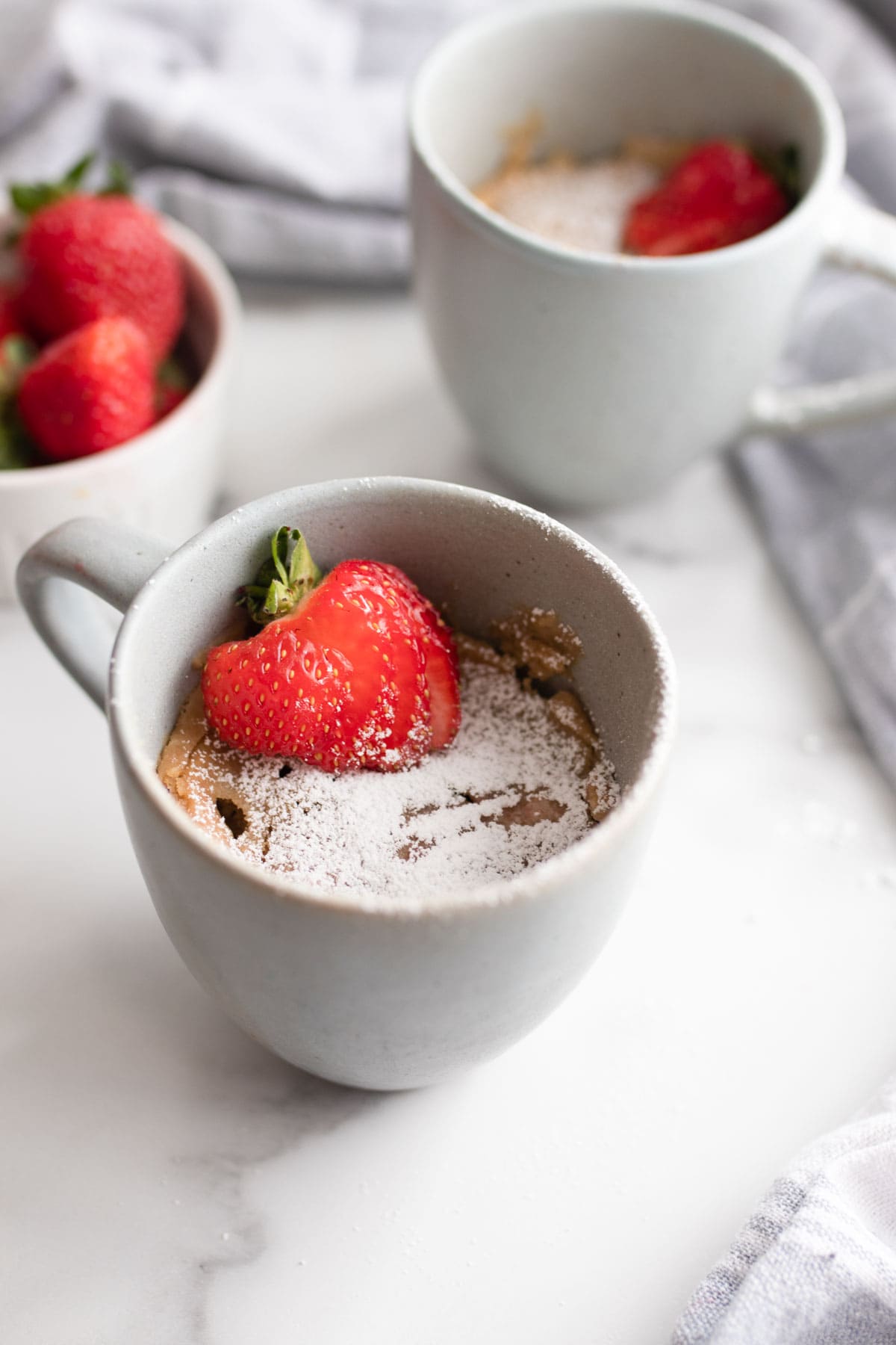Microwave mug cake with powdered sugar and strawberries on top.