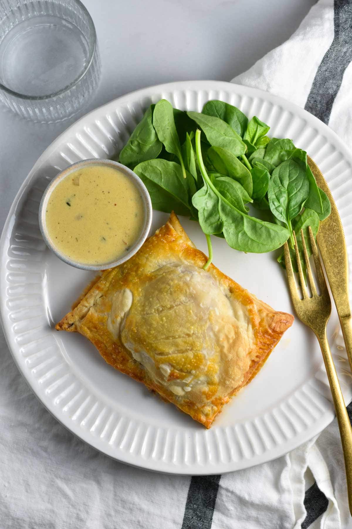 Chicken wellington on a plate with a green salad and dijon sauce.