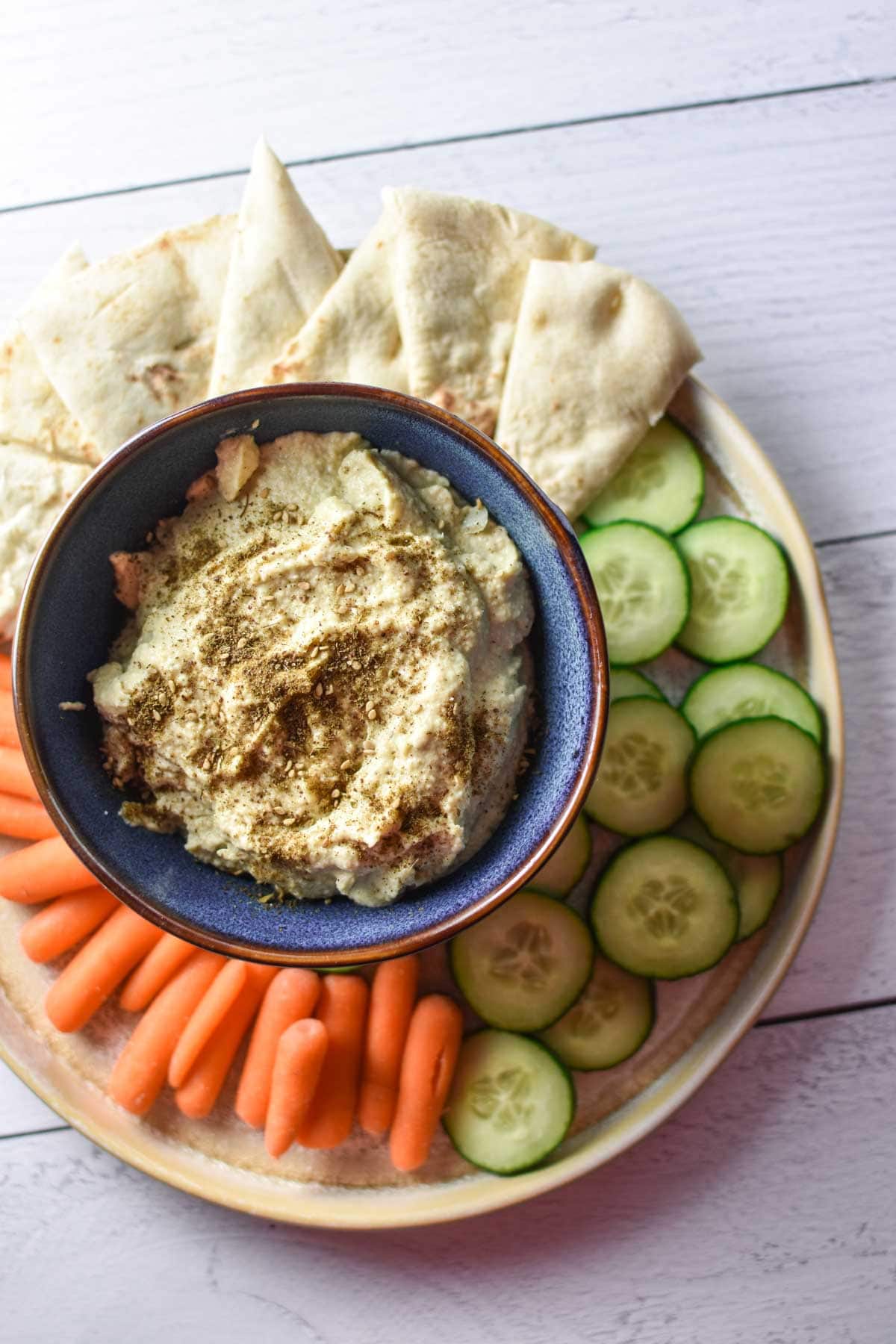 Hummus in a blue bowl next to vegetables.