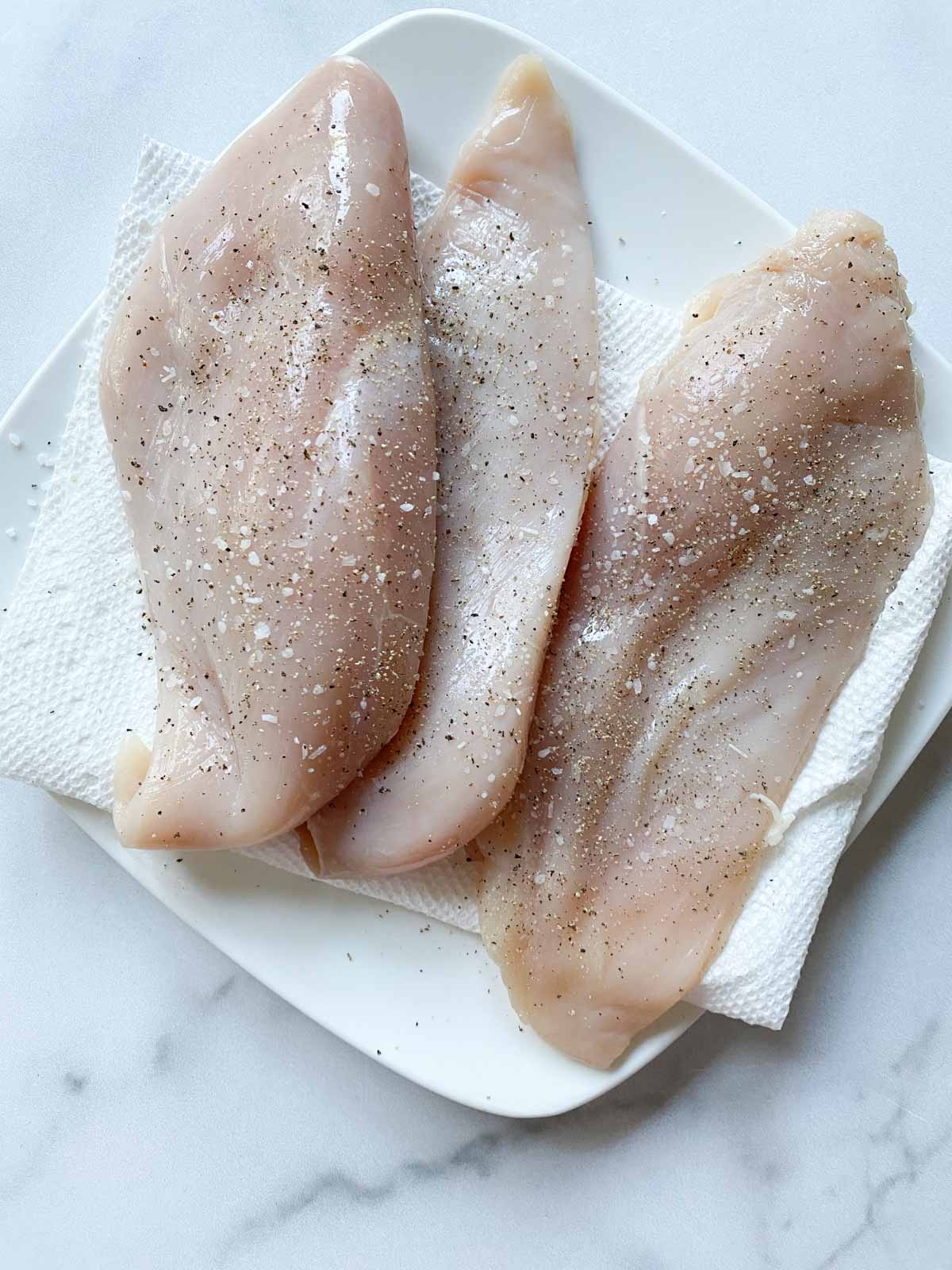 Raw chicken breasts seasoned on a plate.