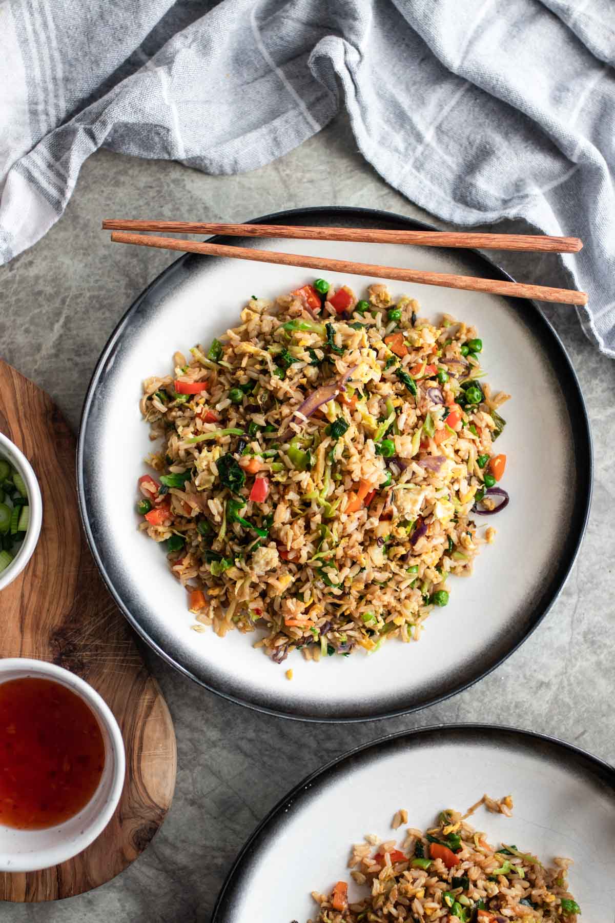 Two bowls of fried rice next to chopsticks and sweet chili sauce.
