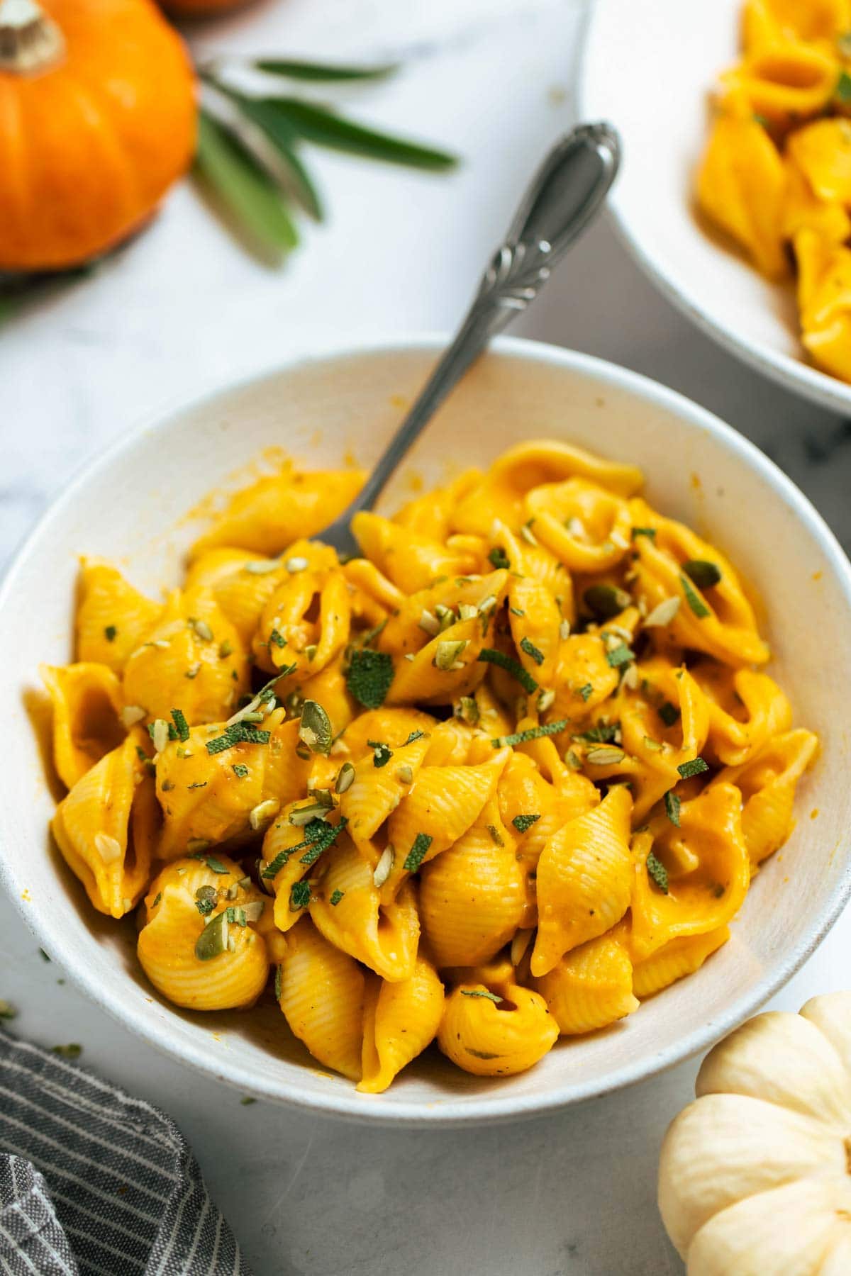 Pumpkin and sage pasta in a bowl with a spoon next to pumpkins.