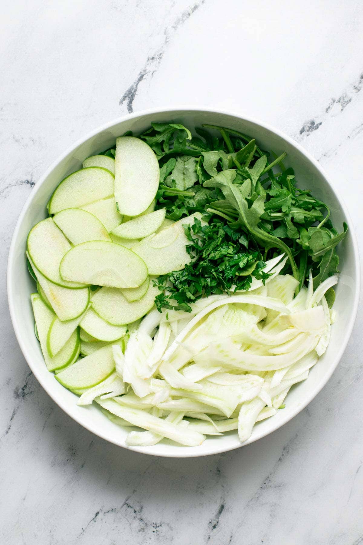A bowl with shaved fennel, apples, and parsley.
