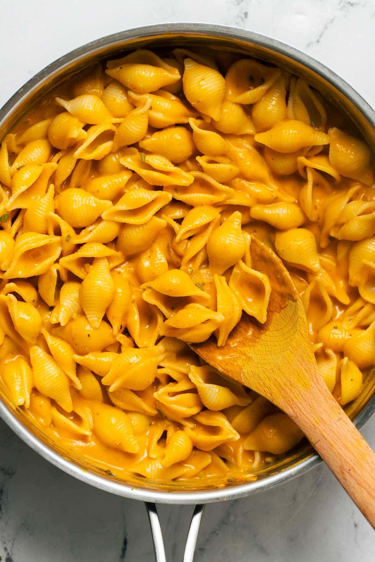 Stirring creamy pasta shells with a wood spoon.