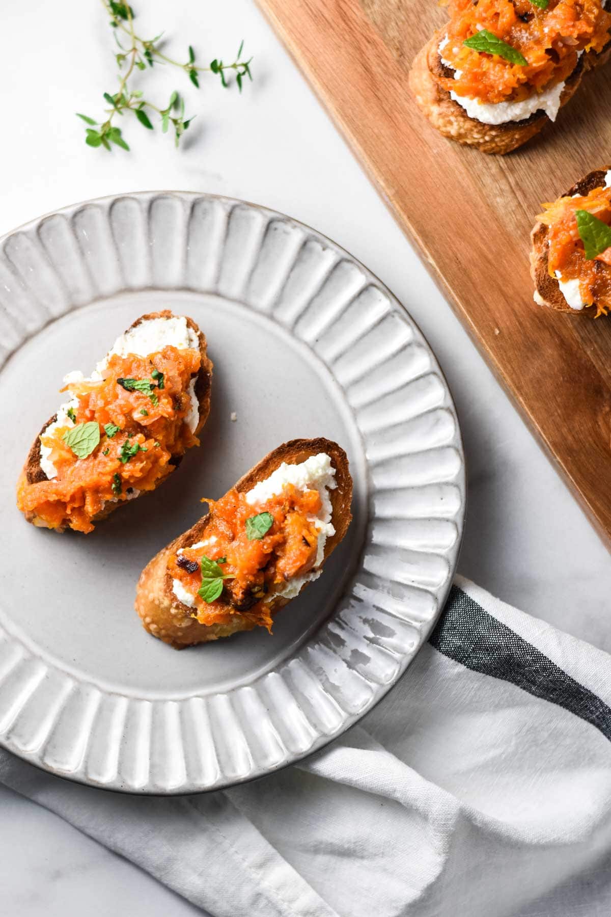 A plate of butternut squash appetizers next to a cutting board with crostini.