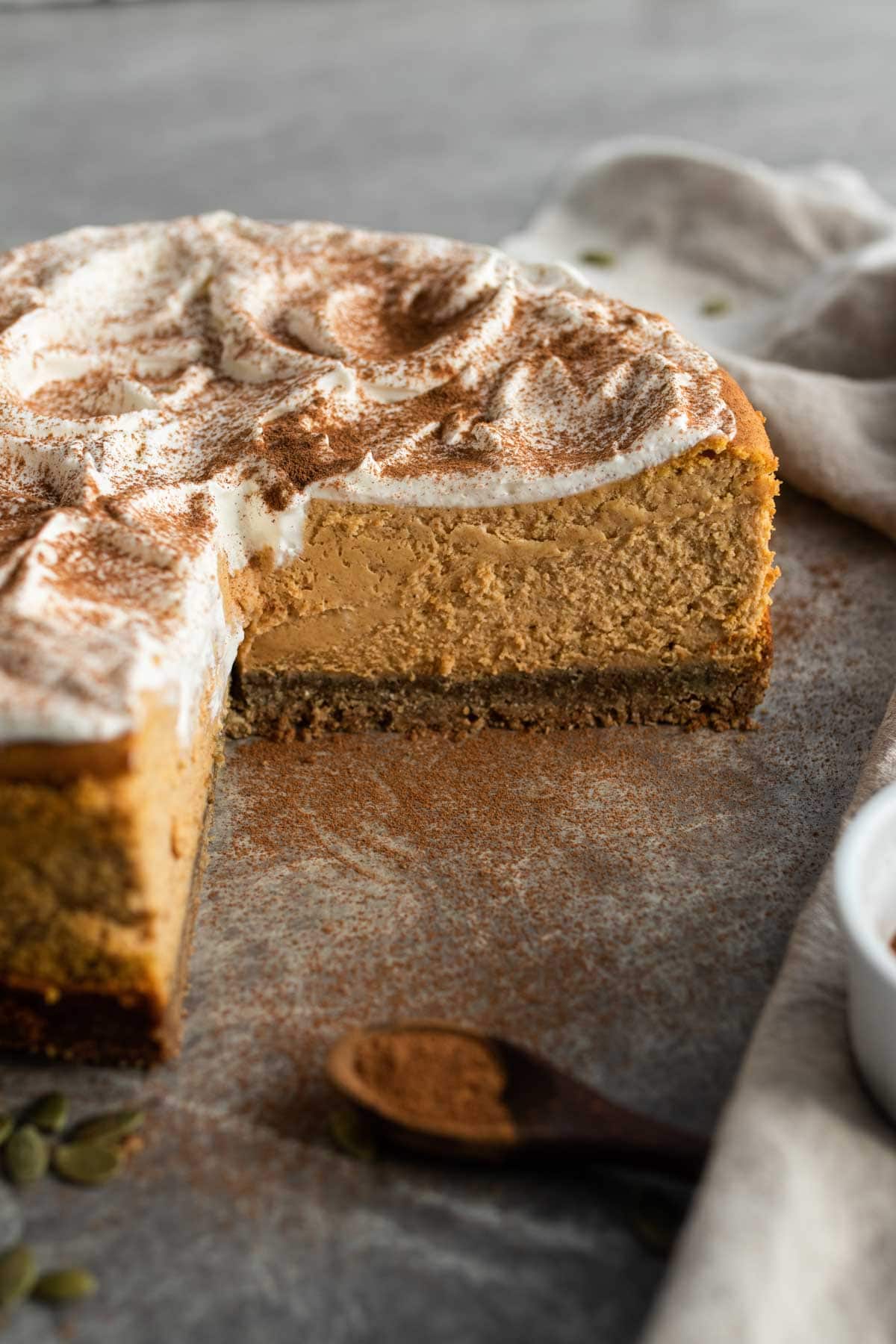 A whole cheesecake sliced with a big cut out, sprinkled with cinnamon and spices. 