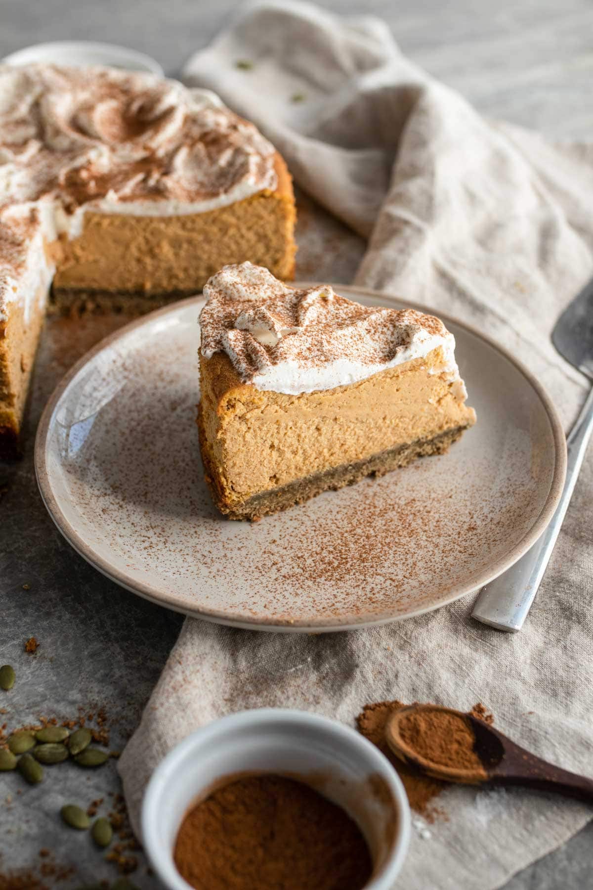 A pumpkin cheesecake slice on a plate dusted with cinnamon.