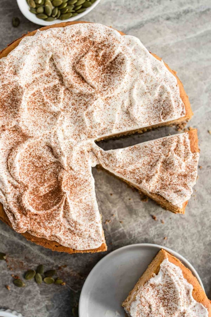 A sliced pumpkin cheesecake with whipped cream and spices on top.