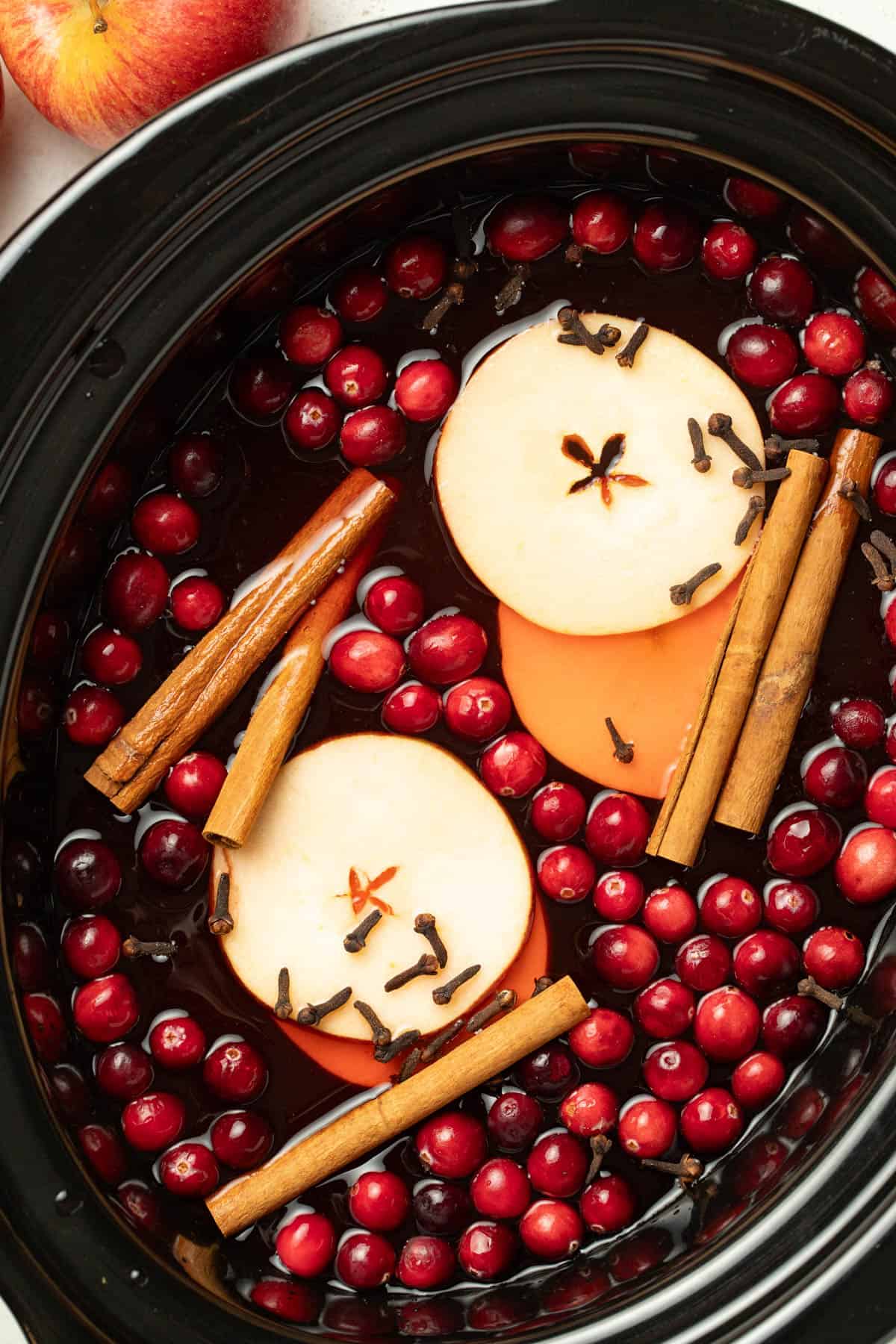 Apples, cloves, cinnamon sticks, and cranberries in a slow cooker with wassail. 