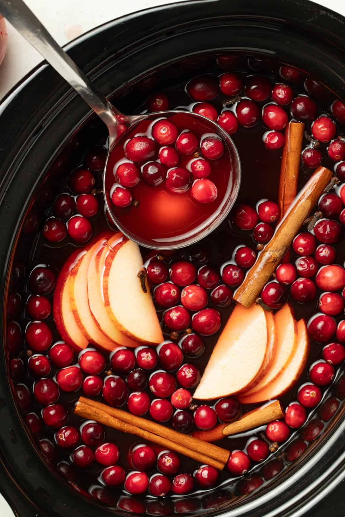 Using a ladle to remove the wassail from the slow cooker.