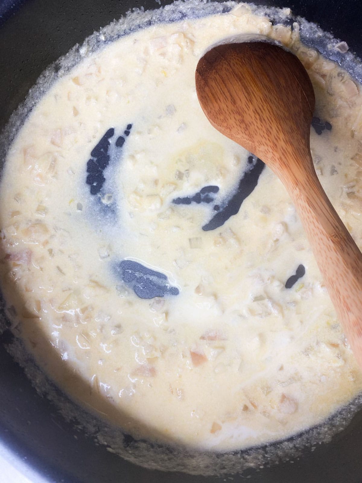 Cream sauce thickening in a pan with a spoon showing how thick it should be.