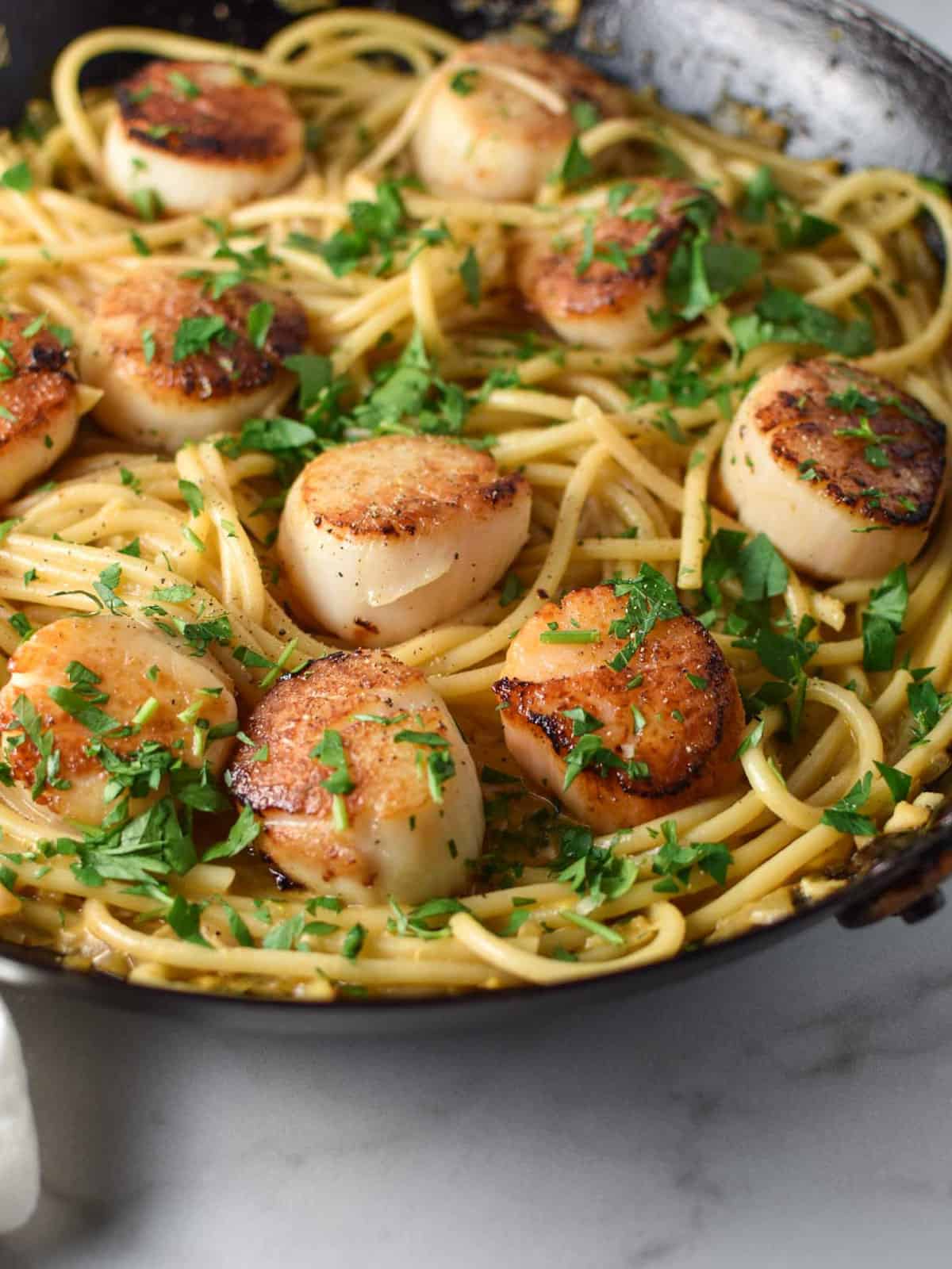 Adding scallops into the pan with linguine and cream sauce. 