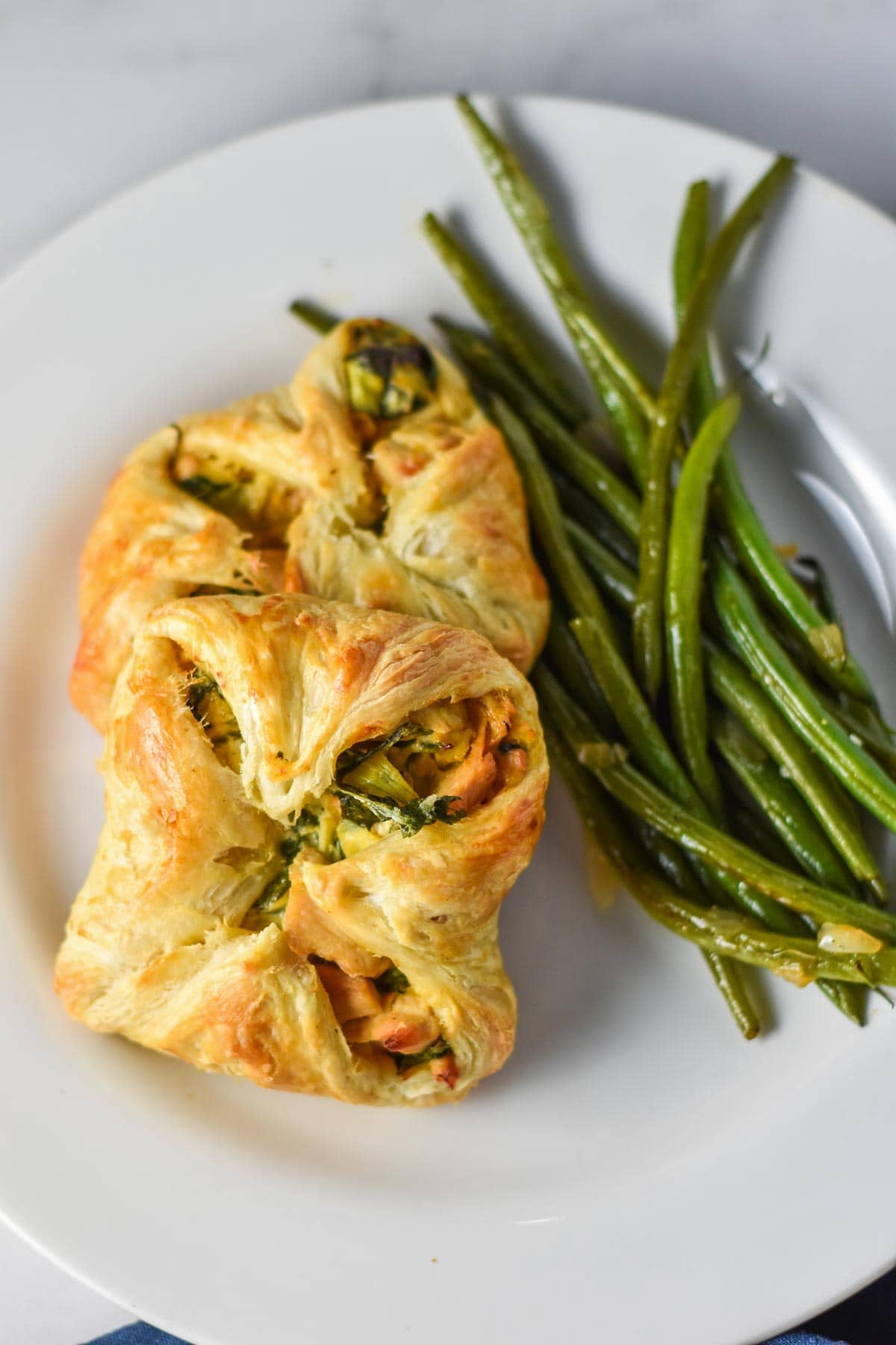 Two chicken in puff pastries next to green beans.