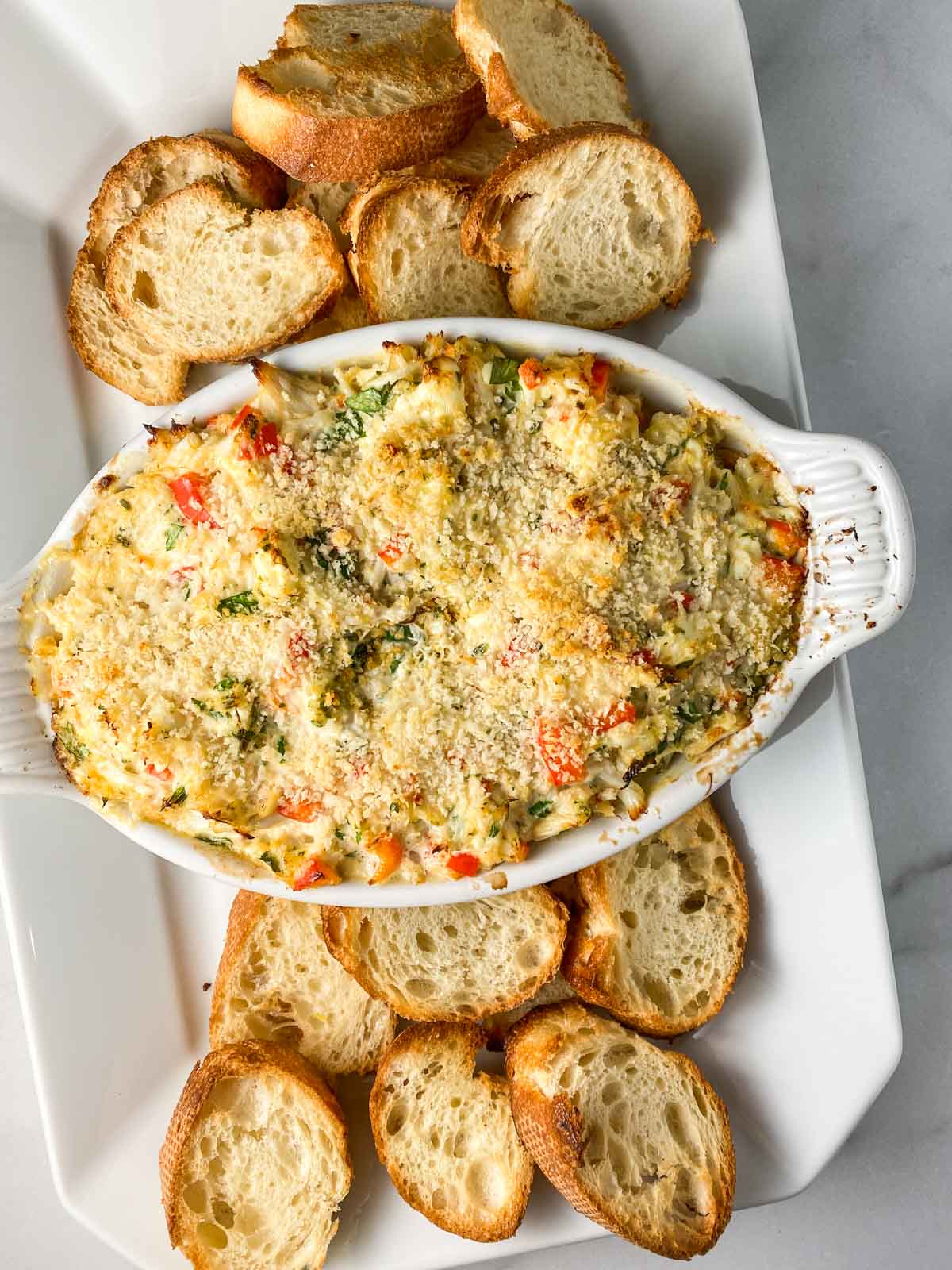 Crab dip in a white bowl with crostini around it.