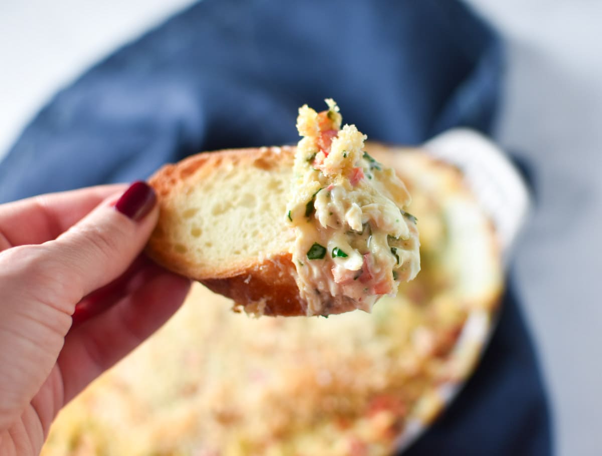 A hand holding a piece of bread topped with crab dip.