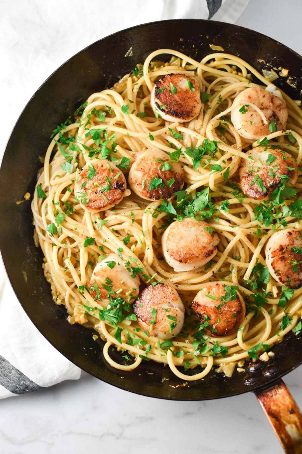 A creamy pasta with seared scallops in an iron pan.