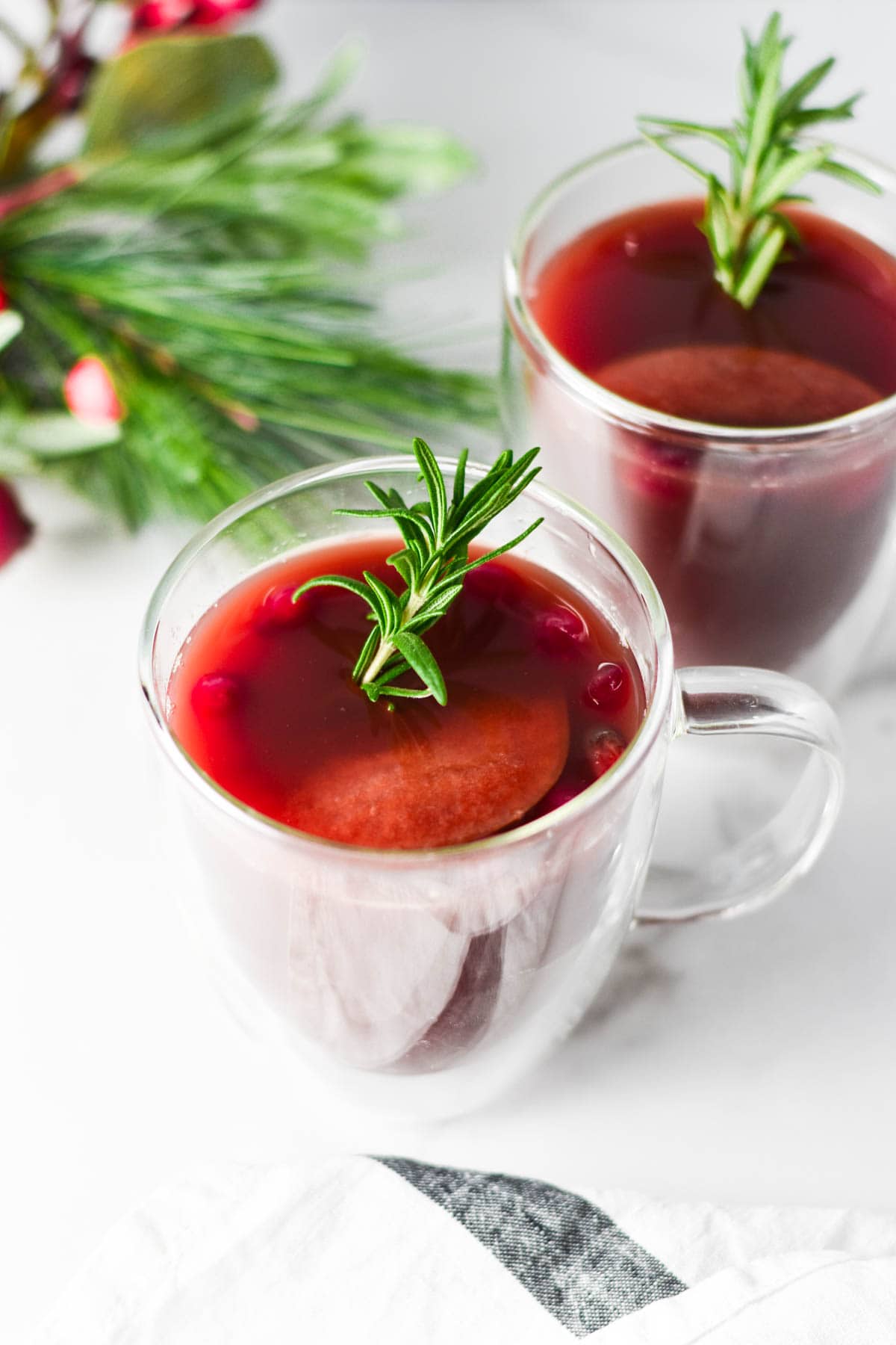 Cranberry wassail cups next to a Christmas tree. 