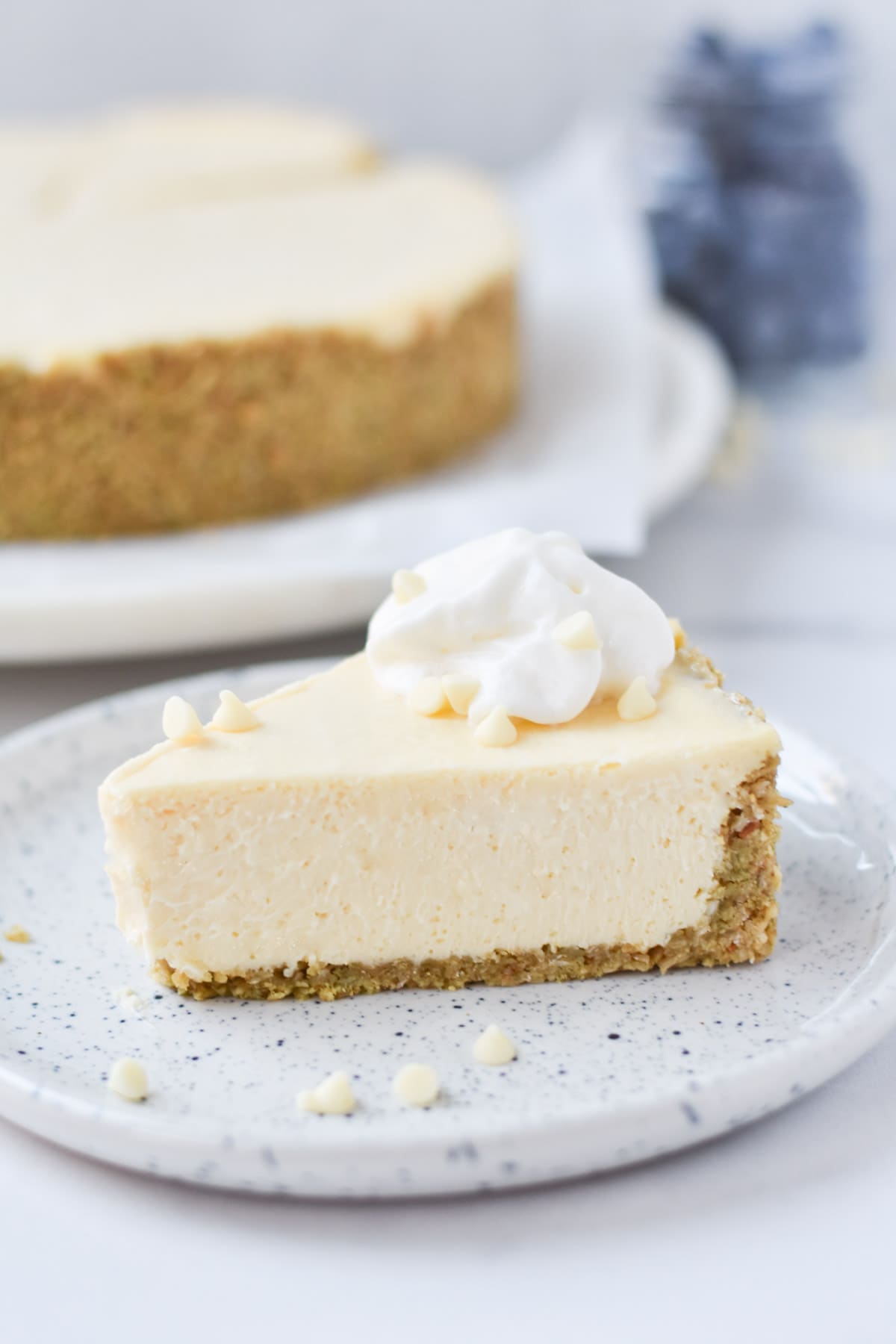 A slice of white chocolate cheesecake with white chocolate sprinkled around.