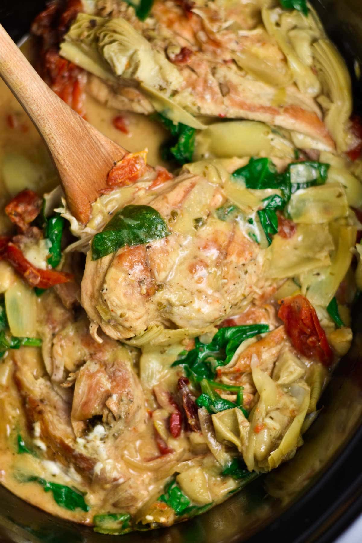 Creamy chicken with artichokes and spinach on a serving spoon.