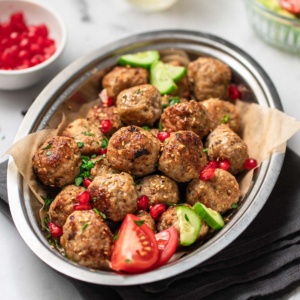 Chicken meatballs in a bowl with tomatoes, cucumber and pomegranate seeds.