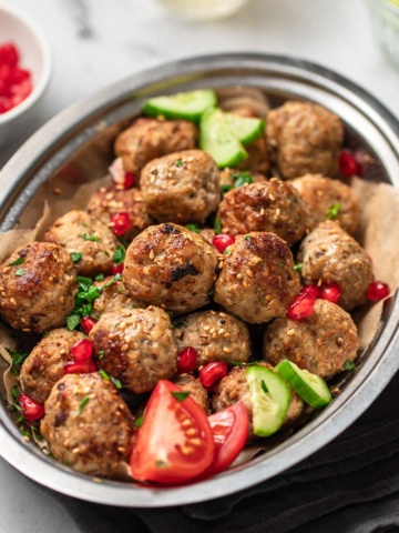 Chicken meatballs in a bowl with tomatoes, cucumber and pomegranate seeds.