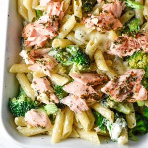 Creamy pasta topped with broccoli and salmon in a baking dish.