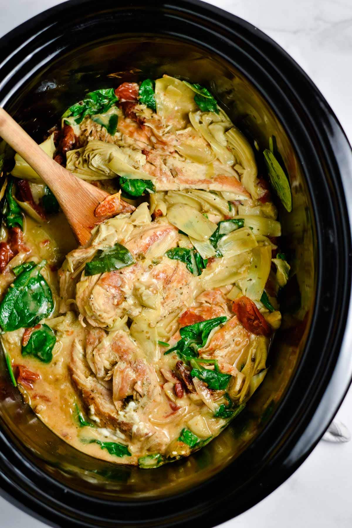 Creamy Tuscan chicken in a crockpot with a spoon.