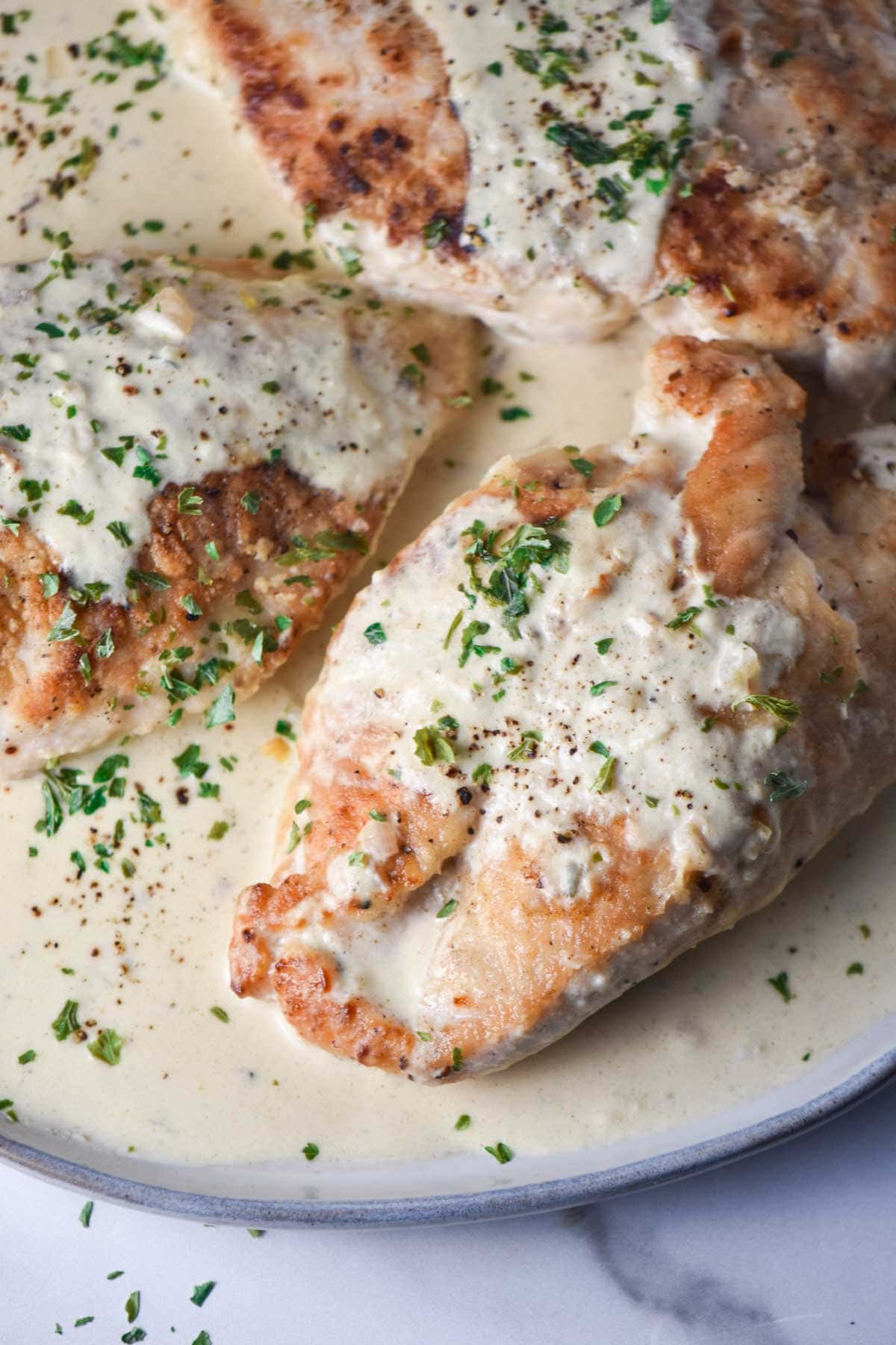 Three chicken breasts on a plate with sauce and parsley.