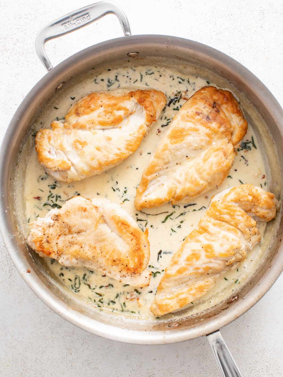 Seared chicken breasts sitting on top of a creamy boursin sauce in a stainless steel pan.