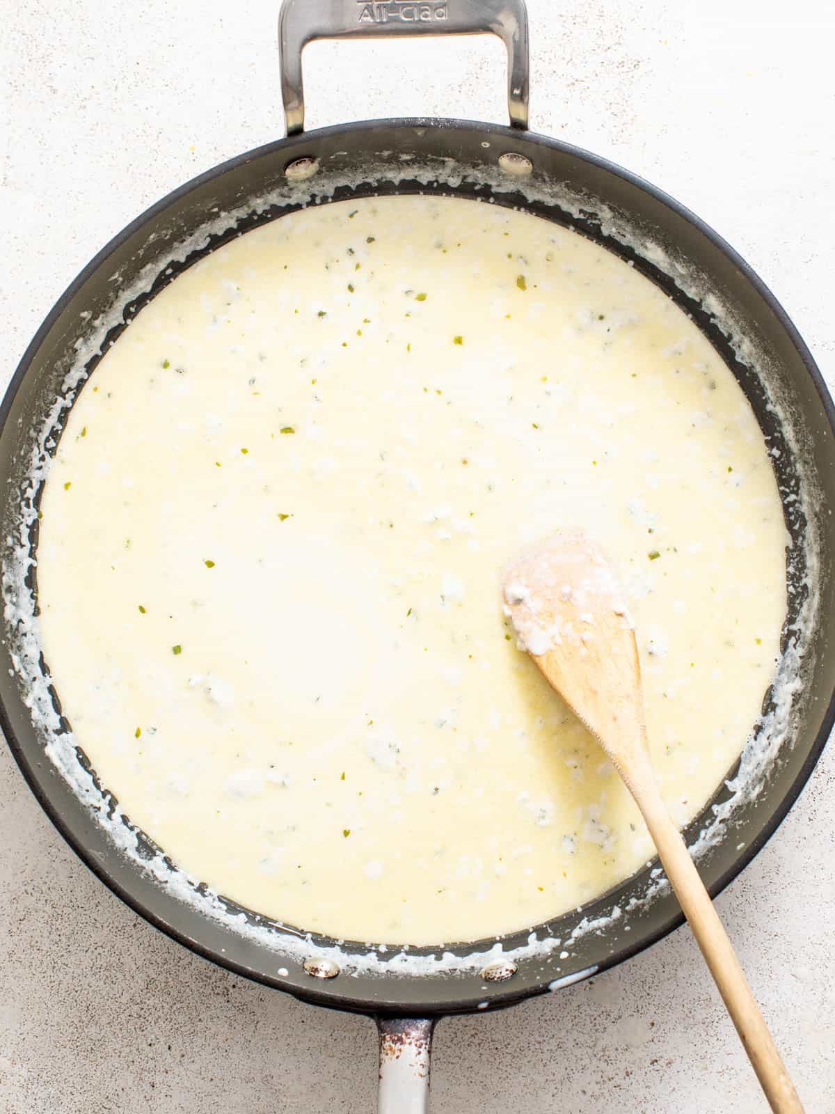 A boursin cream sauce for chicken in a stainless steel pan with a wood spoon.
