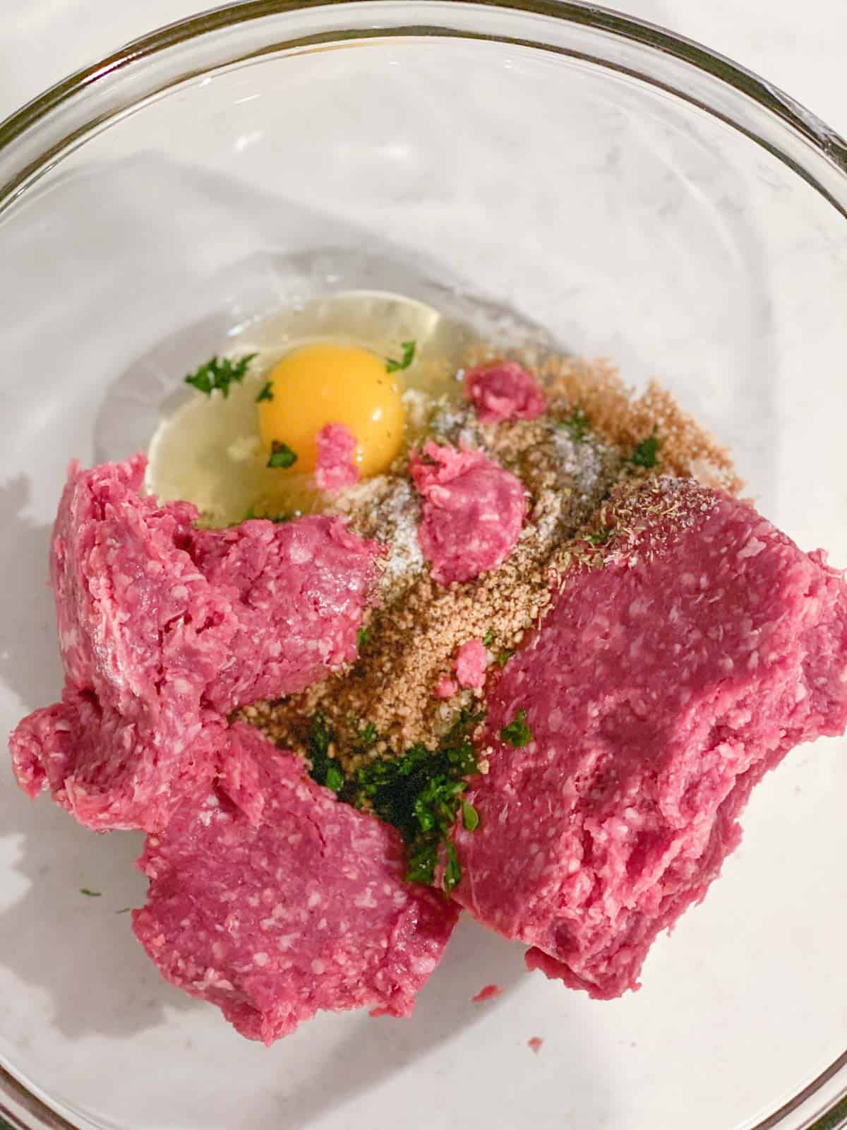 Raw meat being mixed with egg and spices.