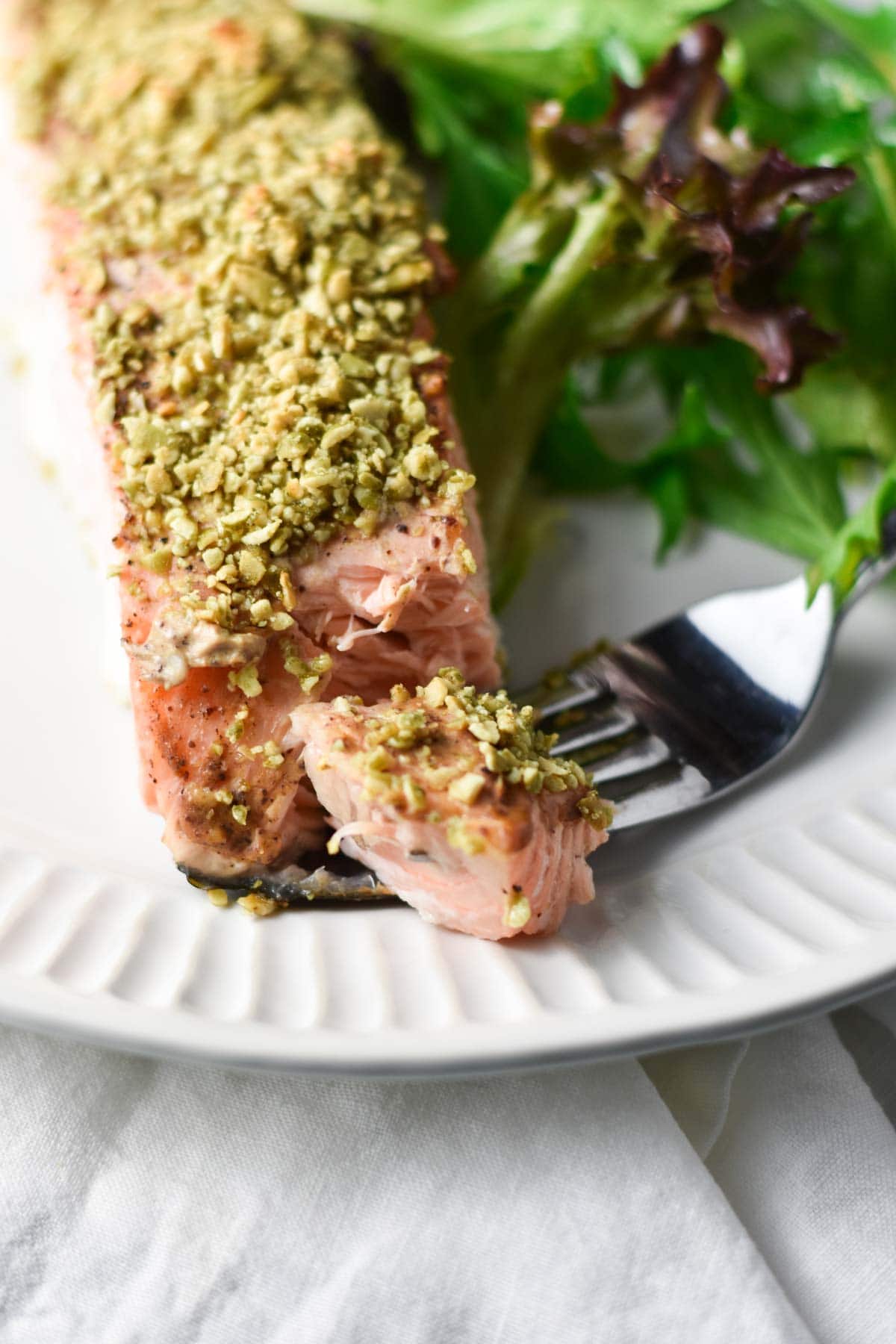 A fork with a bite of salmon next to a salad. 